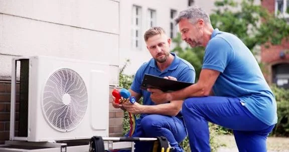 Two technicians checking an outdoor air conditioner with gauges and a tablet